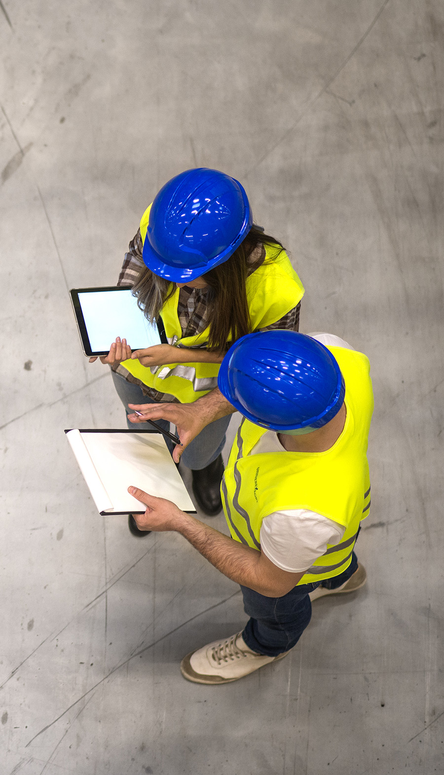 top-view-two-industrial-workers-wearing-hardhats-reflective-jackets-holding-tablet-checklist-gray-concrete-floor